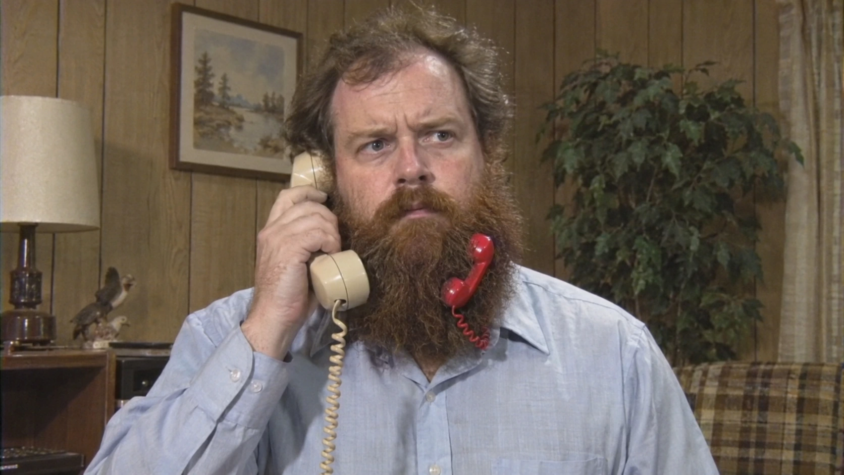 A man takes a very serious phone call while another phone hangs from his beard.